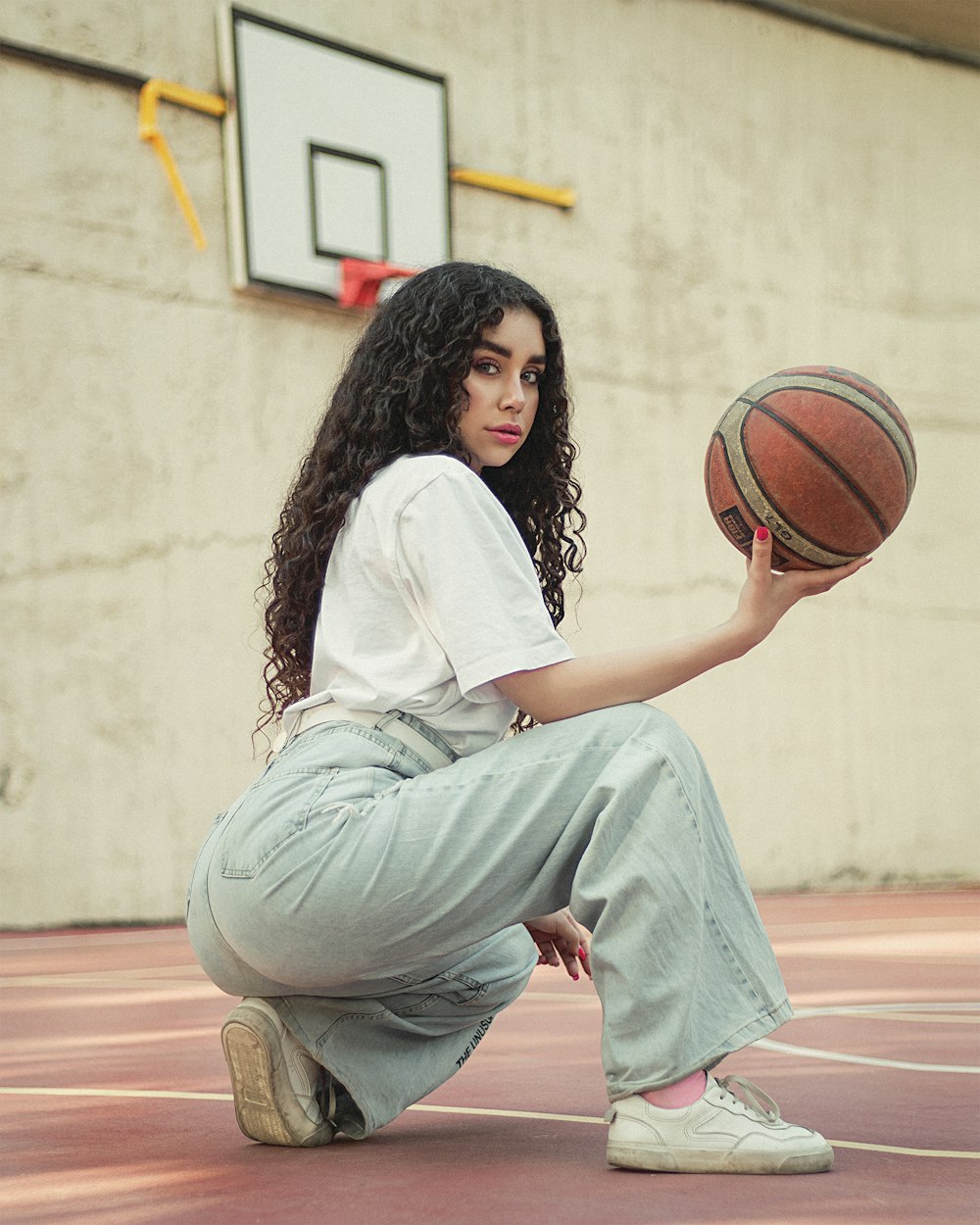 woman in white long sleeve shirt and gray pants sitting on brown wooden floor holding basketball