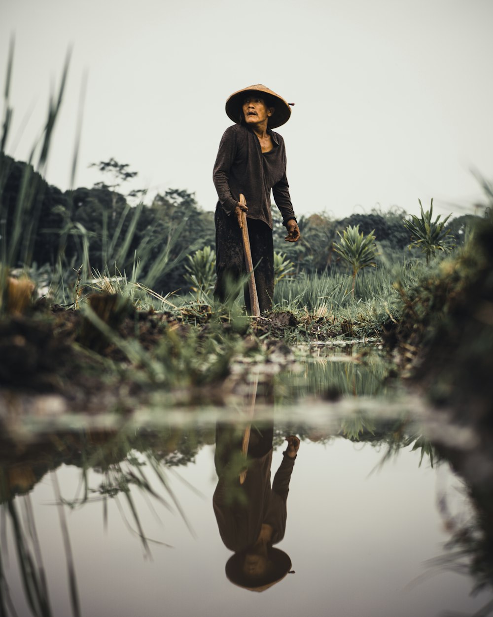 woman in black coat standing on green grass field near lake during daytime