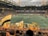 A large, packed stadium during a soccer match with fans waving yellow and black flags, creating a lively and vibrant atmosphere. The crowd is dense, with many people visibly engaged and cheering. Players can be seen on the field, along with some officials and staff.