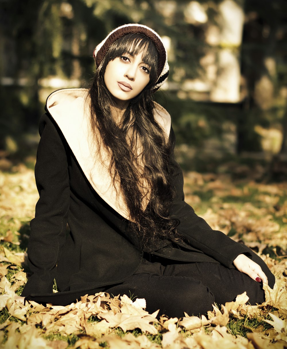 woman in black blazer and white scarf sitting on ground with dried leaves