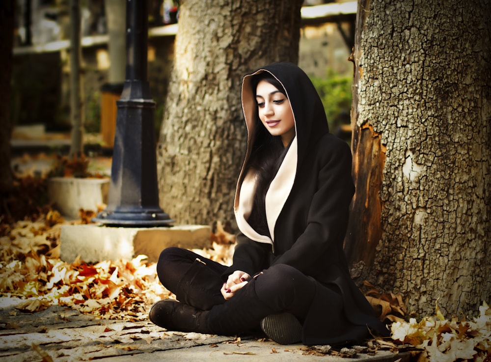 woman in black long sleeve shirt and black pants sitting on ground with dried leaves