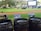 A grassy outdoor area features a large inflatable movie screen with people sitting on blankets to watch an open-air film. In the foreground, three wooden trash bins are labeled for landfill, compostable, and recyclable waste, promoting waste separation and environmental awareness. The environment is surrounded by trees and a relaxed atmosphere is evident.