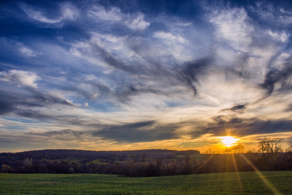 Champ d’herbe verte sous un ciel nuageux au coucher du soleil