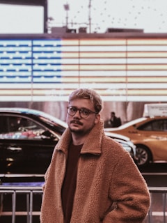 man in brown coat standing near black car during daytime