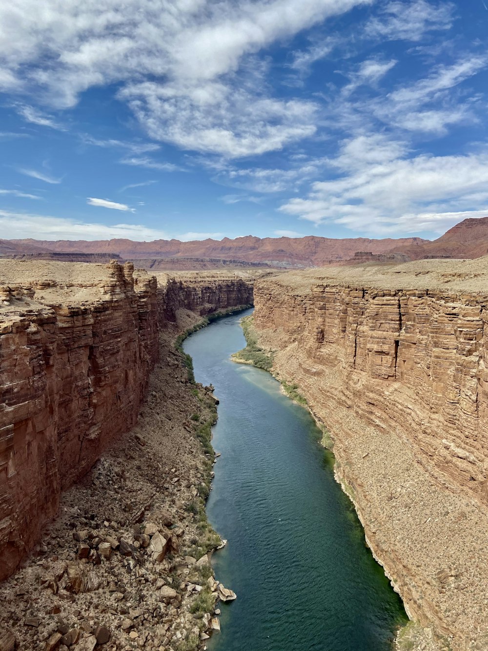 brown rocky mountain beside river under blue sky during daytime