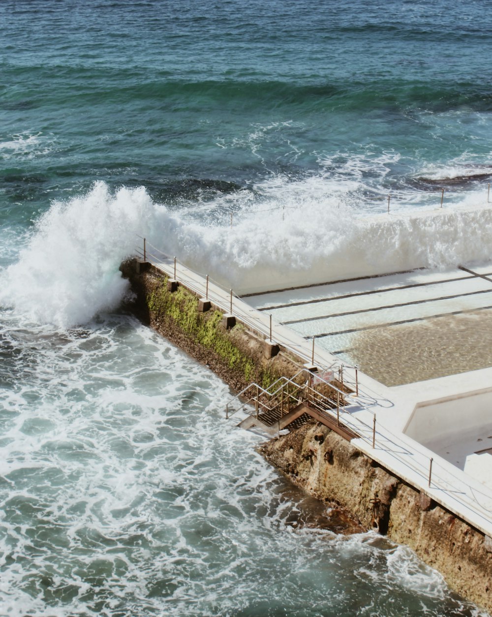 parede de concreto branco perto das ondas do mar durante o dia