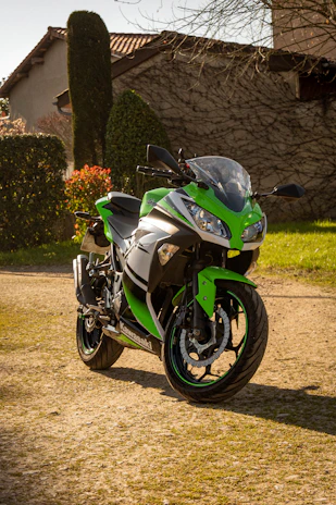A shiny black and green Kawasaki motorcycle parked under cherry blossom trees in bloom.