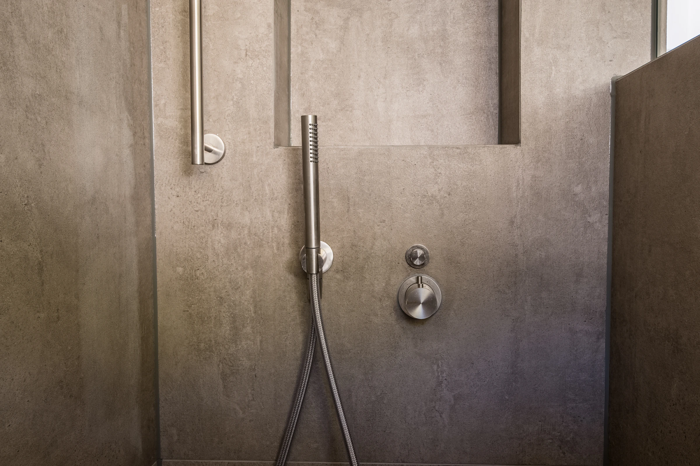 Handheld shower and a slim stainless grab bar on a stone wall