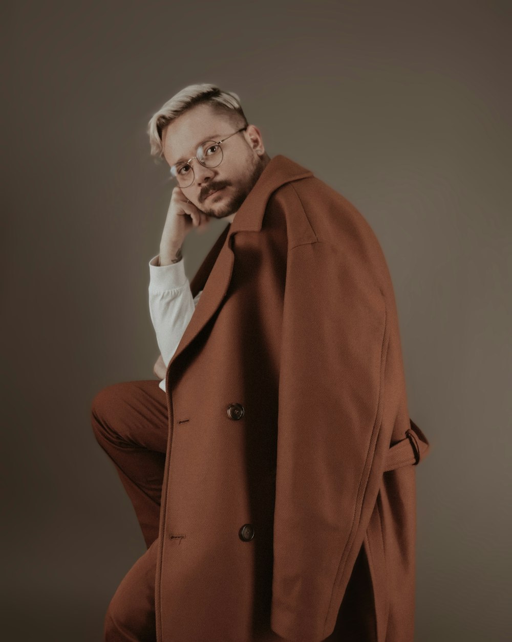 man in brown coat holding his chin