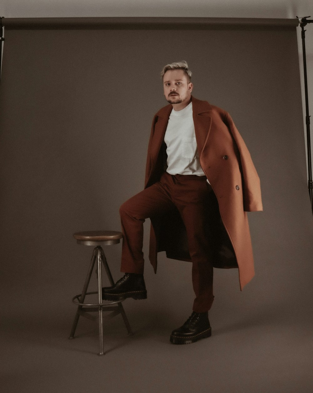 man in brown coat and black pants sitting on chair