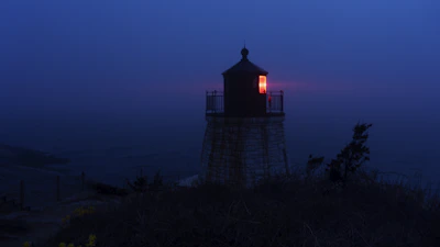 A lone, spectral lighthouse casting a faint glow over misty, black waters.