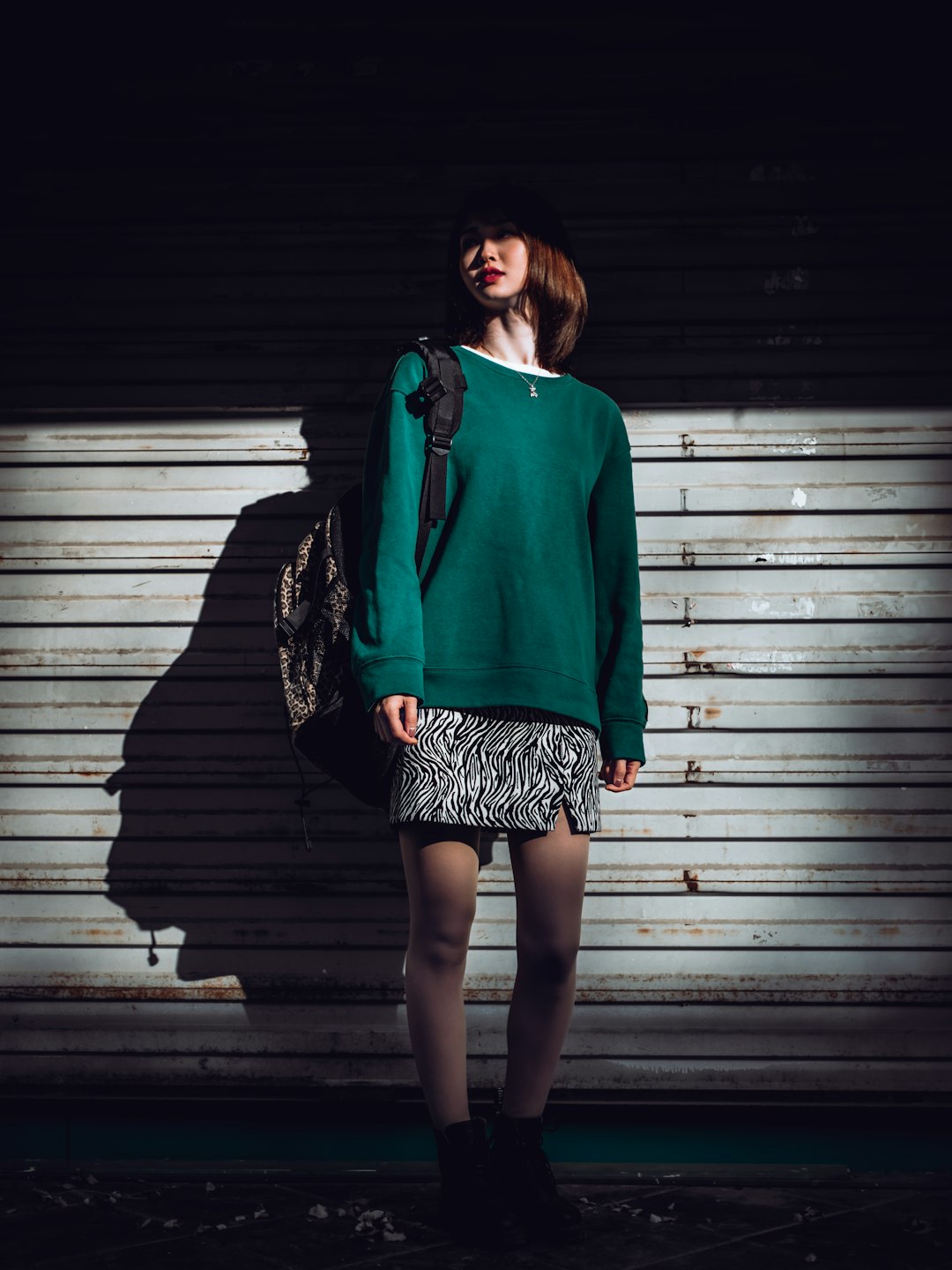woman in green long sleeve shirt and black and white skirt standing in front of gray