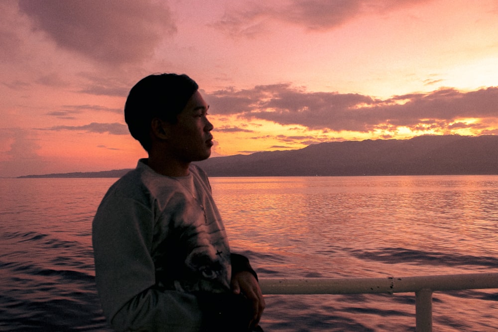 man in gray sweater sitting on beach during sunset