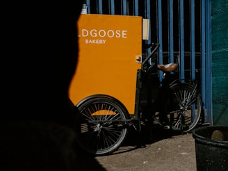 A cheerful delivery bike with a basket full of banana bread boxes parked near a North Shore beach scene.