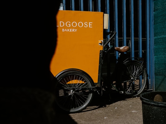 A cheerful delivery bike with a basket full of banana bread boxes parked near a North Shore beach scene.