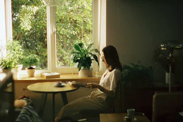 A calm woman sitting at a cozy kitchen table, enjoying a relaxed meal surrounded by soft natural light.