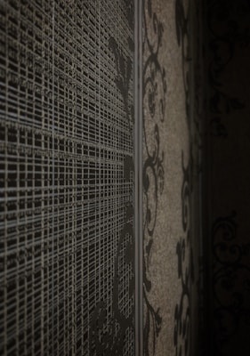 A textured surface features intricate, abstract patterns with fine lines and swirling designs. The wall presents a blend of geometric and ornamental motifs that create a sense of depth and complexity.