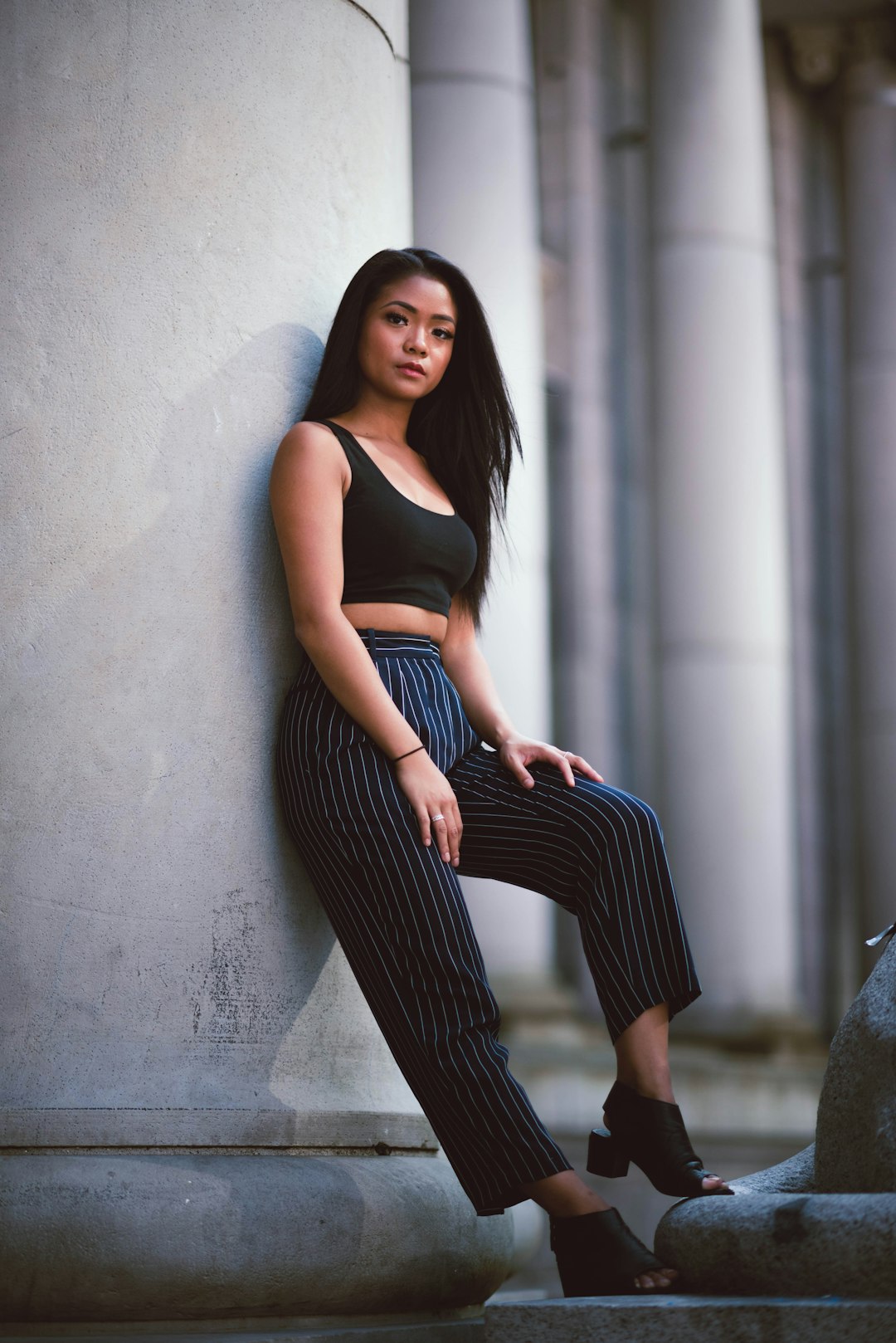 woman in black tank top and black and white striped pants sitting on concrete wall