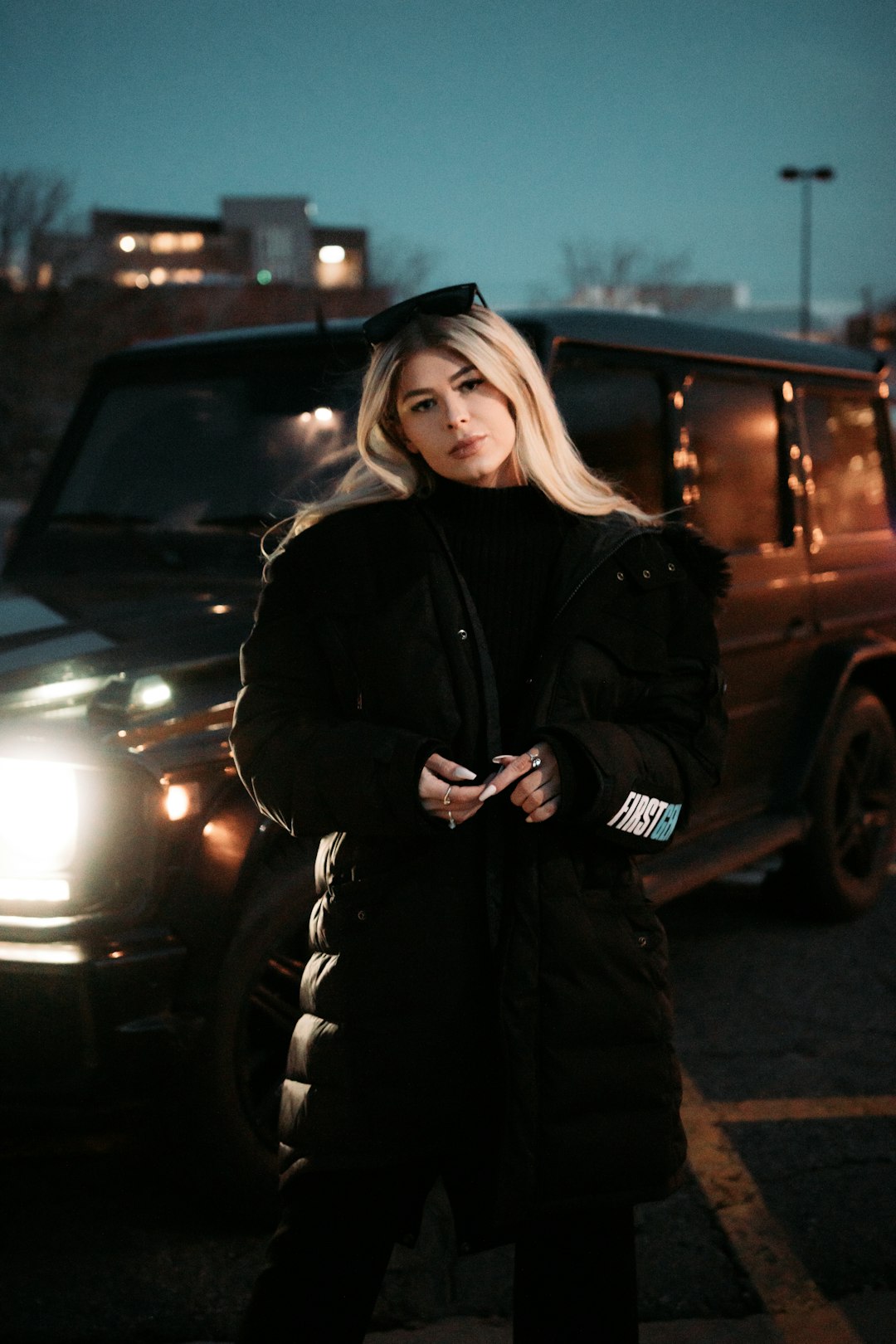 woman in black coat standing beside black car during night time