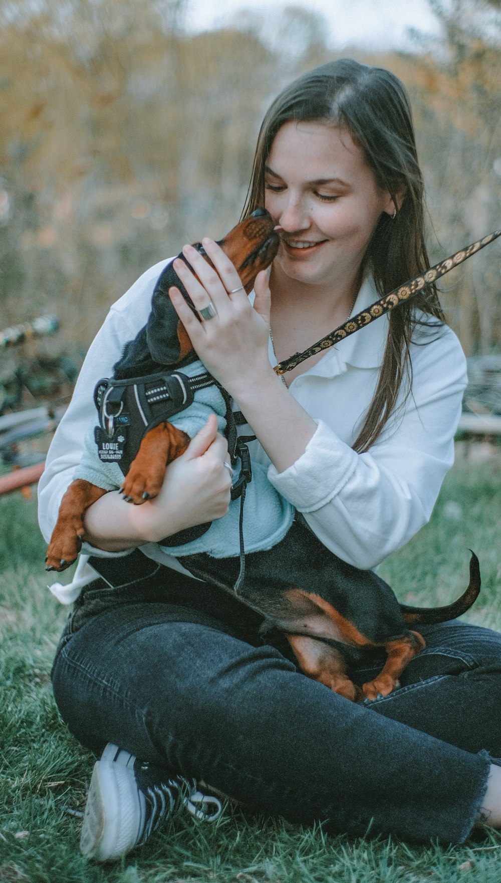 woman in white long sleeve shirt and blue denim jeans holding brown and black dog