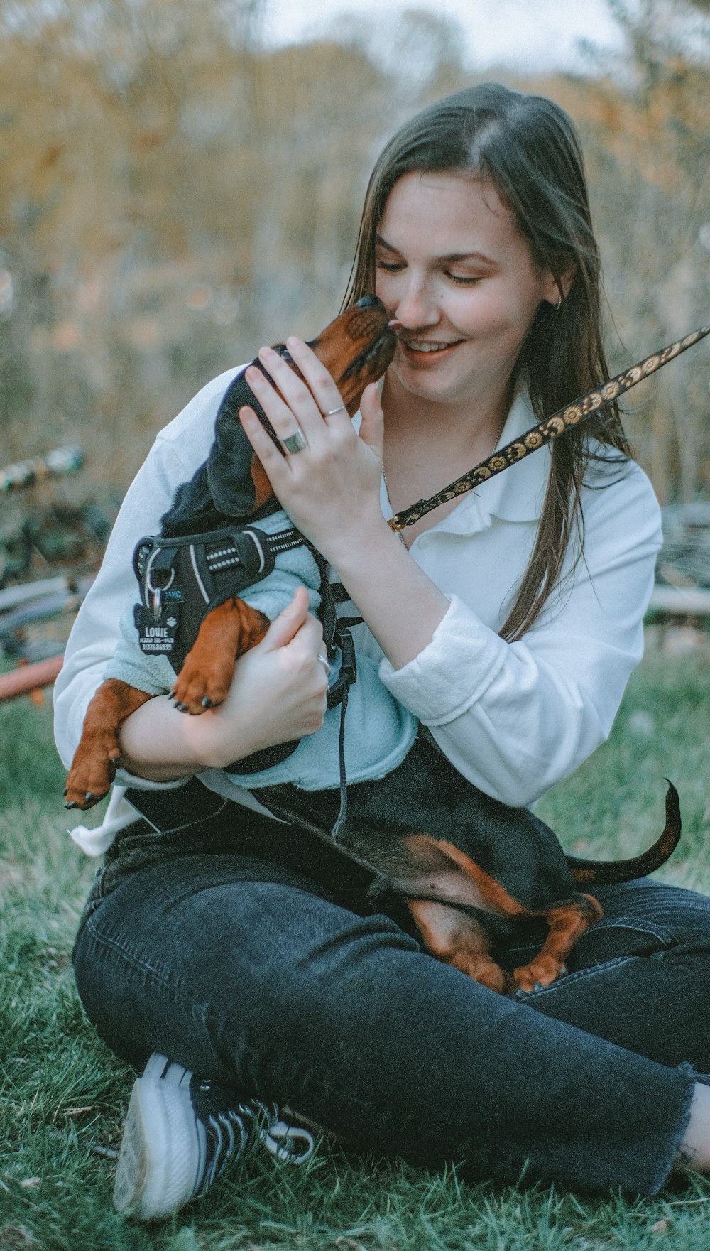 mulher na camisa branca de manga comprida e jeans jeans azuis segurando o cão marrom e preto