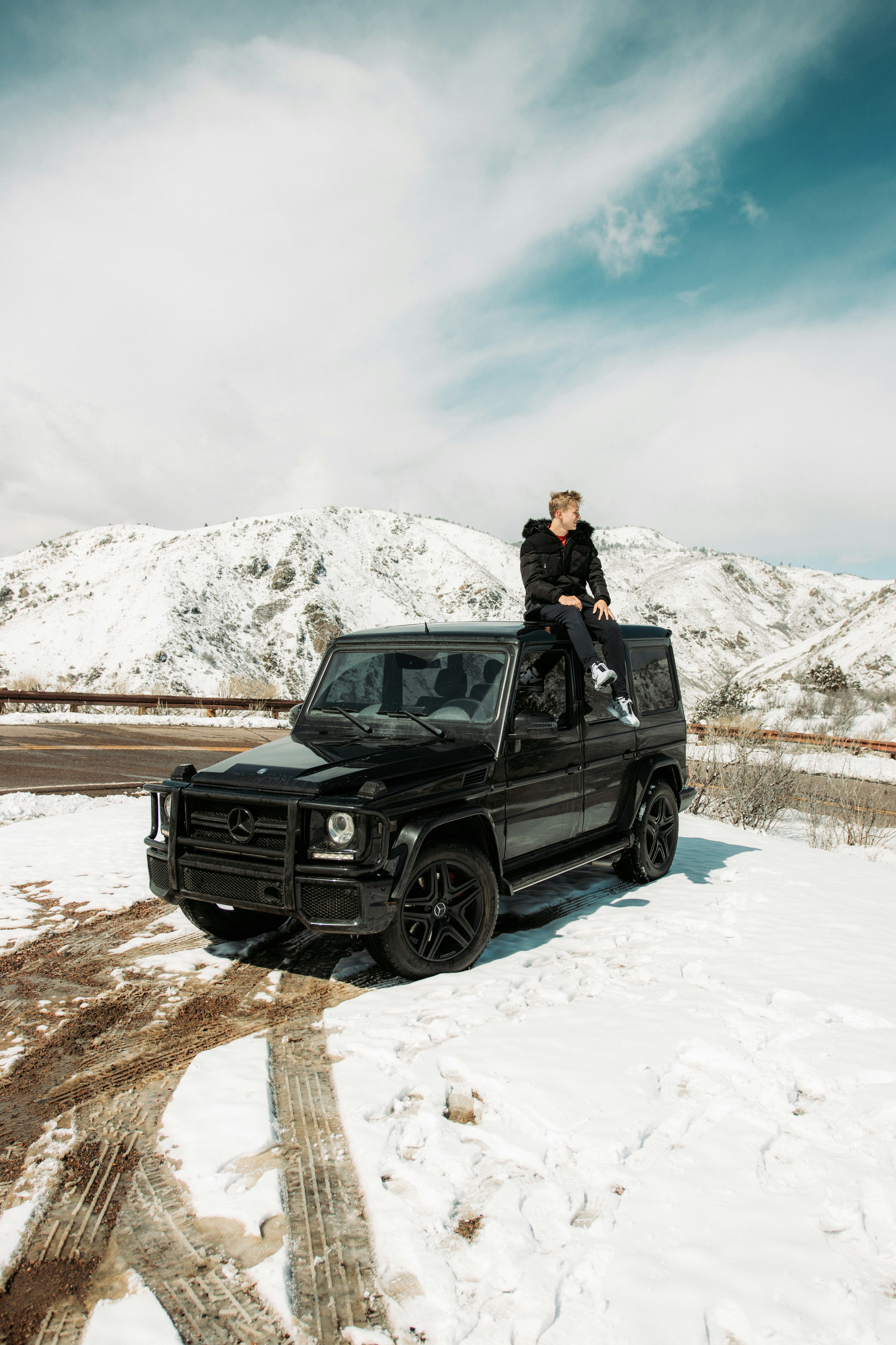 woman in black jacket and black pants sitting on black suv on snow covered ground during