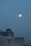 A large full moon is positioned against a clear evening sky. Below it, a modern building with an observatory dome is visible, suggesting a setting for stargazing or astronomical observation.