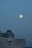 A large full moon is positioned against a clear evening sky. Below it, a modern building with an observatory dome is visible, suggesting a setting for stargazing or astronomical observation.