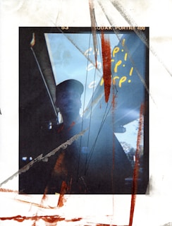 A mixed-media image with a partially visible person in silhouette against a light background, overlaid with abstract scribbles and handwritten text in yellow. The photograph has a raw, textured feel with scratches and splatters along with a visible film frame.