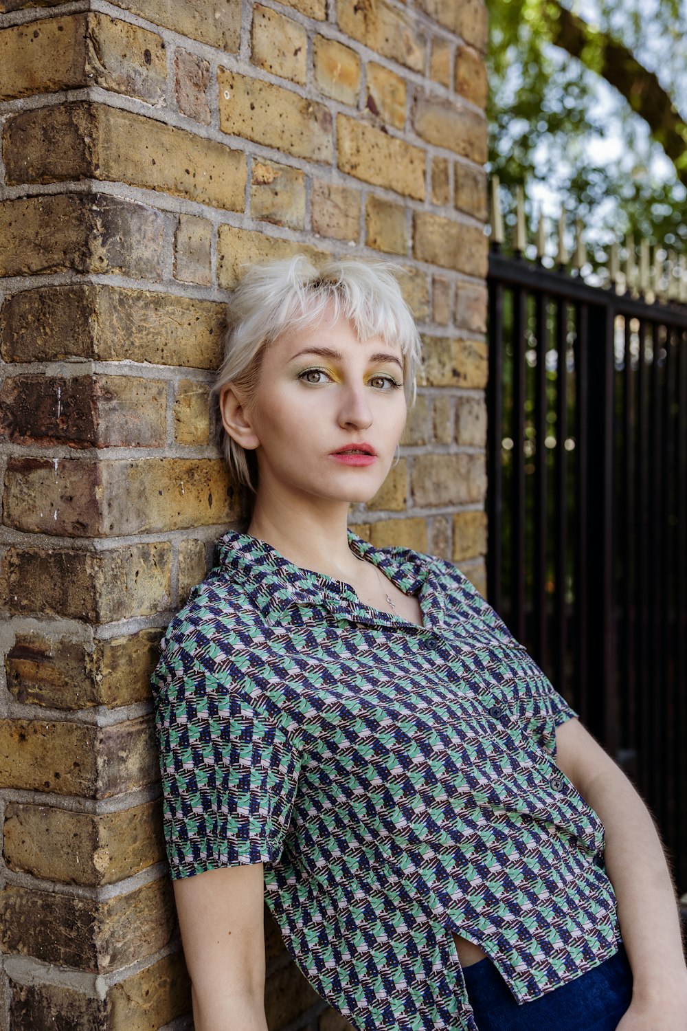 woman in black and white shirt leaning on brown brick wall