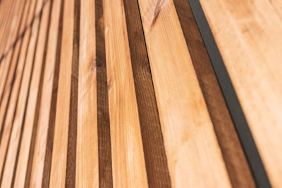 Close-up view of wooden planks arranged in a parallel pattern, showcasing natural textures and variations in wood grain. The planks alternate between lighter and darker shades and run diagonally from the lower left to the upper right.