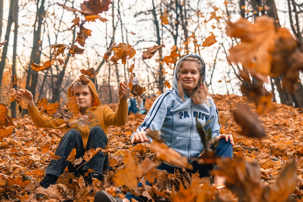 woman in gray and blue hoodie sitting on dried leaves during daytime