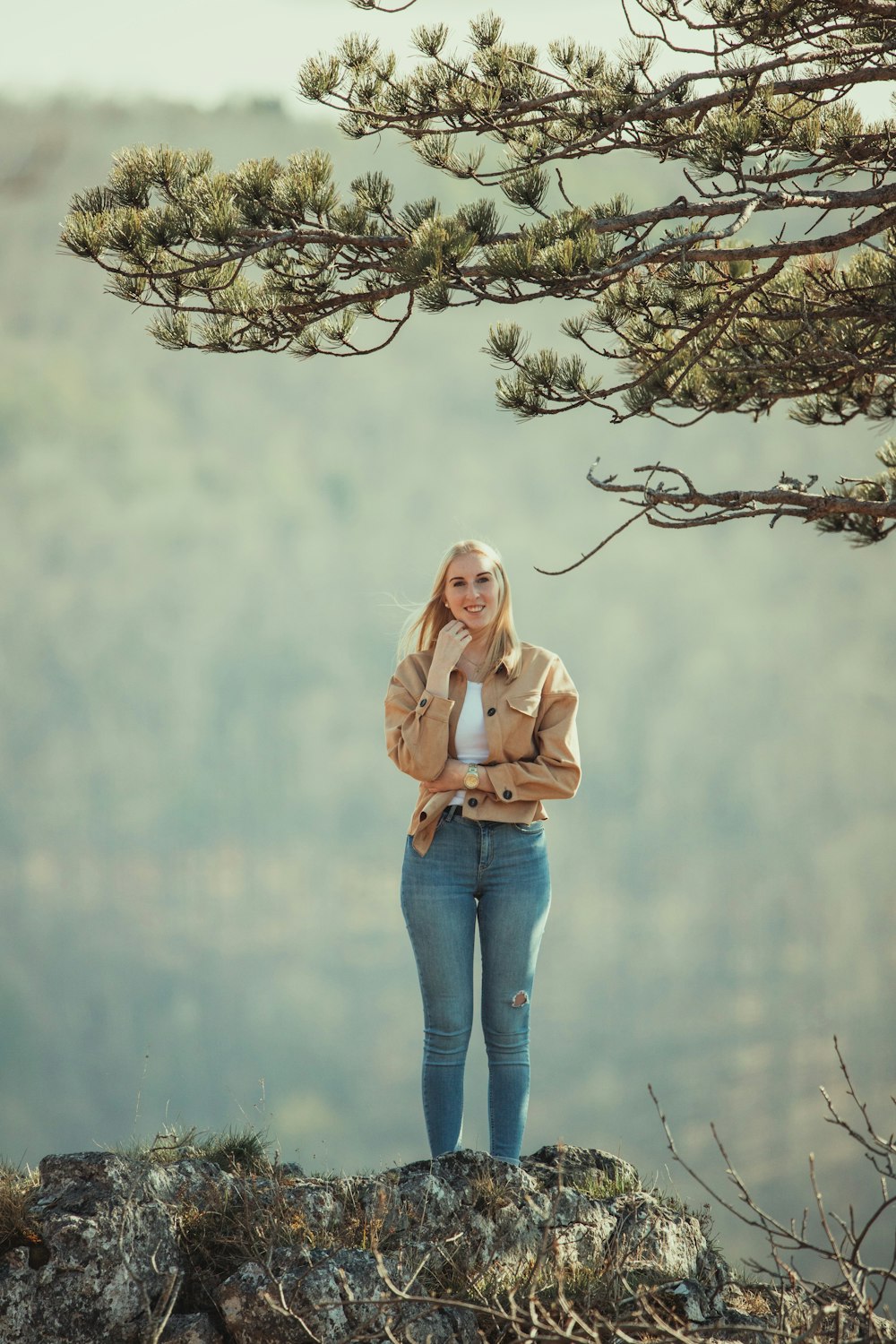 woman in pink long sleeve shirt and blue denim jeans standing on tree branch during daytime