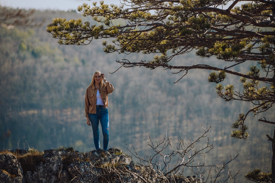 woman in brown jacket and blue denim jeans standing on brown tree branch