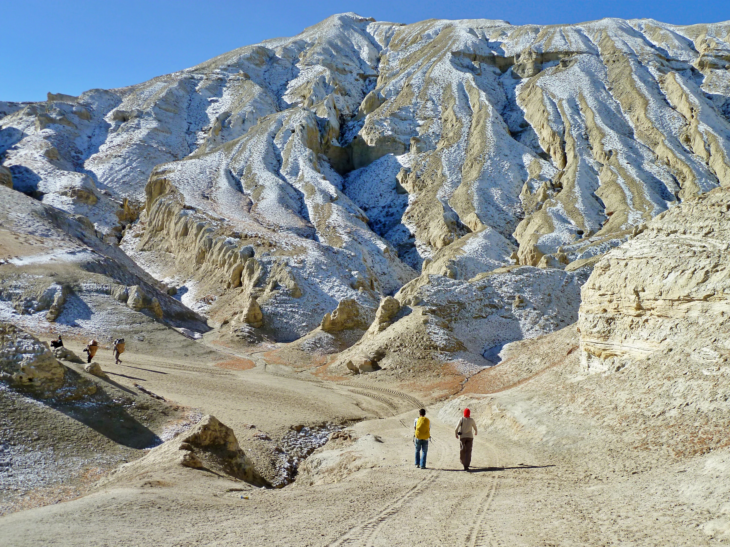 Trekkers walking a sandy trail through the eroded ochre cliffs and high desert of Upper Mustang, Nepal