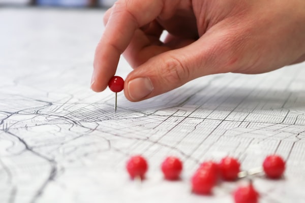 a close-up of a hand pushing a pin into a street map, with several other pins in the foreground
