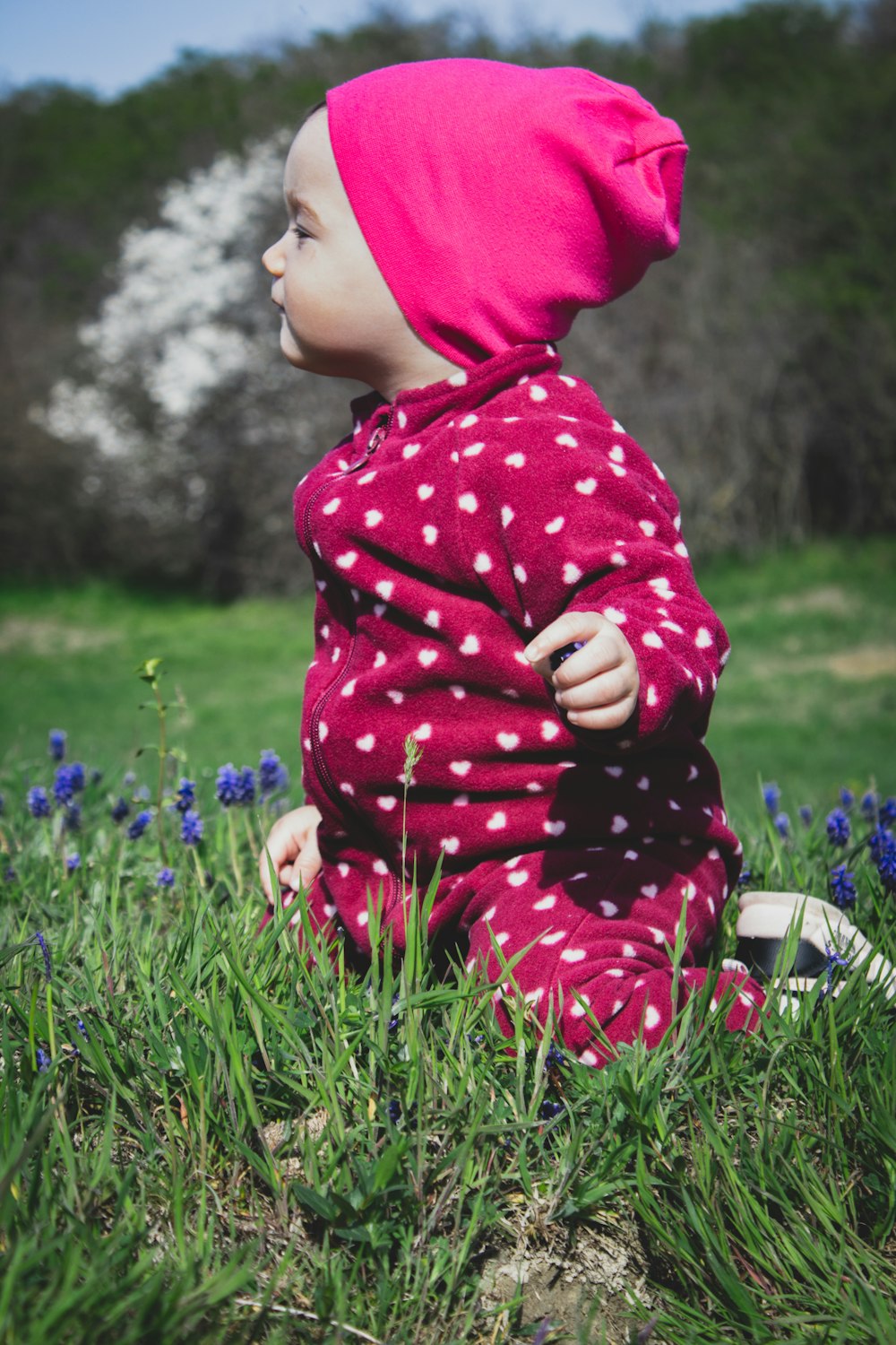 girl in red and white polka dot hoodie sitting on green grass field during daytime