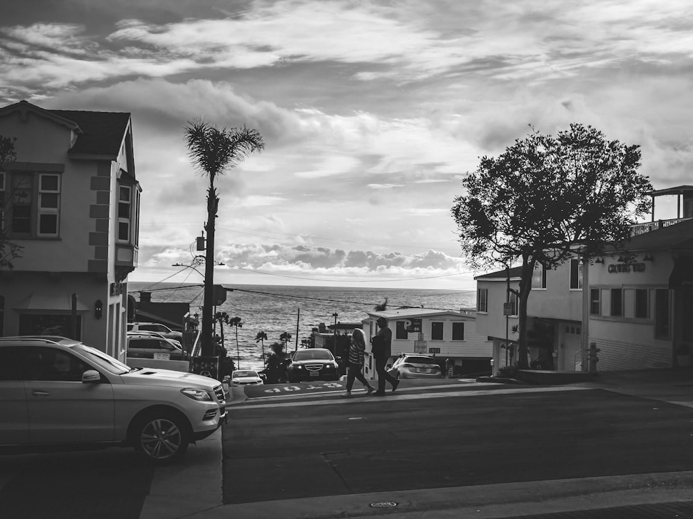 grayscale photo of people walking on sidewalk near cars and buildings