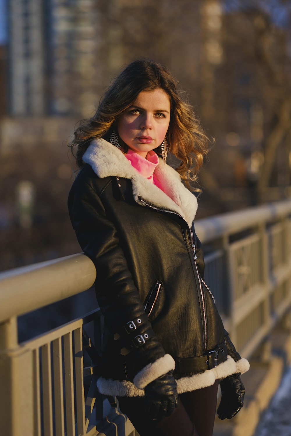 woman in black leather jacket standing near brown wooden fence during daytime