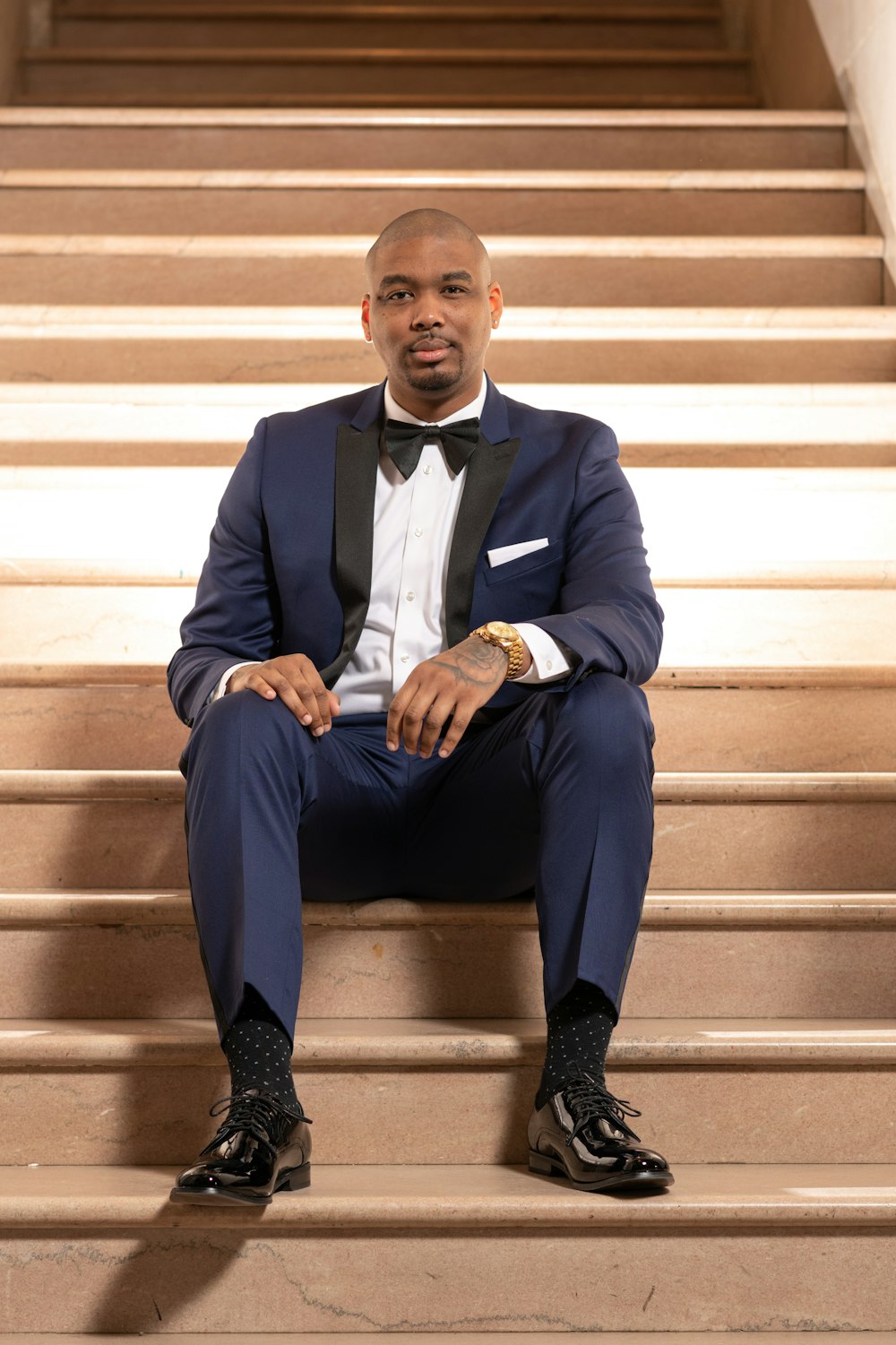 man in black suit sitting on brown concrete stairs