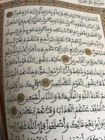 A page from a religious text written in Arabic calligraphy. The text is framed with an ornate floral border, and several verses are marked with decorative golden circles containing numbers.