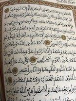 A page from a religious text written in Arabic calligraphy. The text is framed with an ornate floral border, and several verses are marked with decorative golden circles containing numbers.