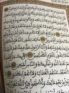 A page from a religious text written in Arabic calligraphy. The text is framed with an ornate floral border, and several verses are marked with decorative golden circles containing numbers.