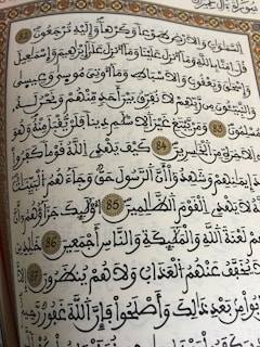 A page from a religious text written in Arabic calligraphy. The text is framed with an ornate floral border, and several verses are marked with decorative golden circles containing numbers.
