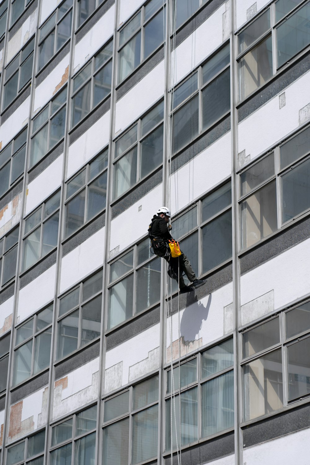 homem em jaqueta preta e calças pretas em pé na frente do edifício da janela de vidro durante o dia