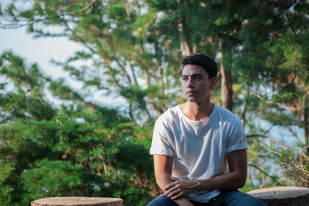 man in white crew neck t-shirt sitting on brown wooden bench during daytime