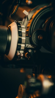 Close-up of a camera rig with various focus gears and equipment components, exhibiting details of lenses, cogwheels, and mechanical parts under warm lighting.