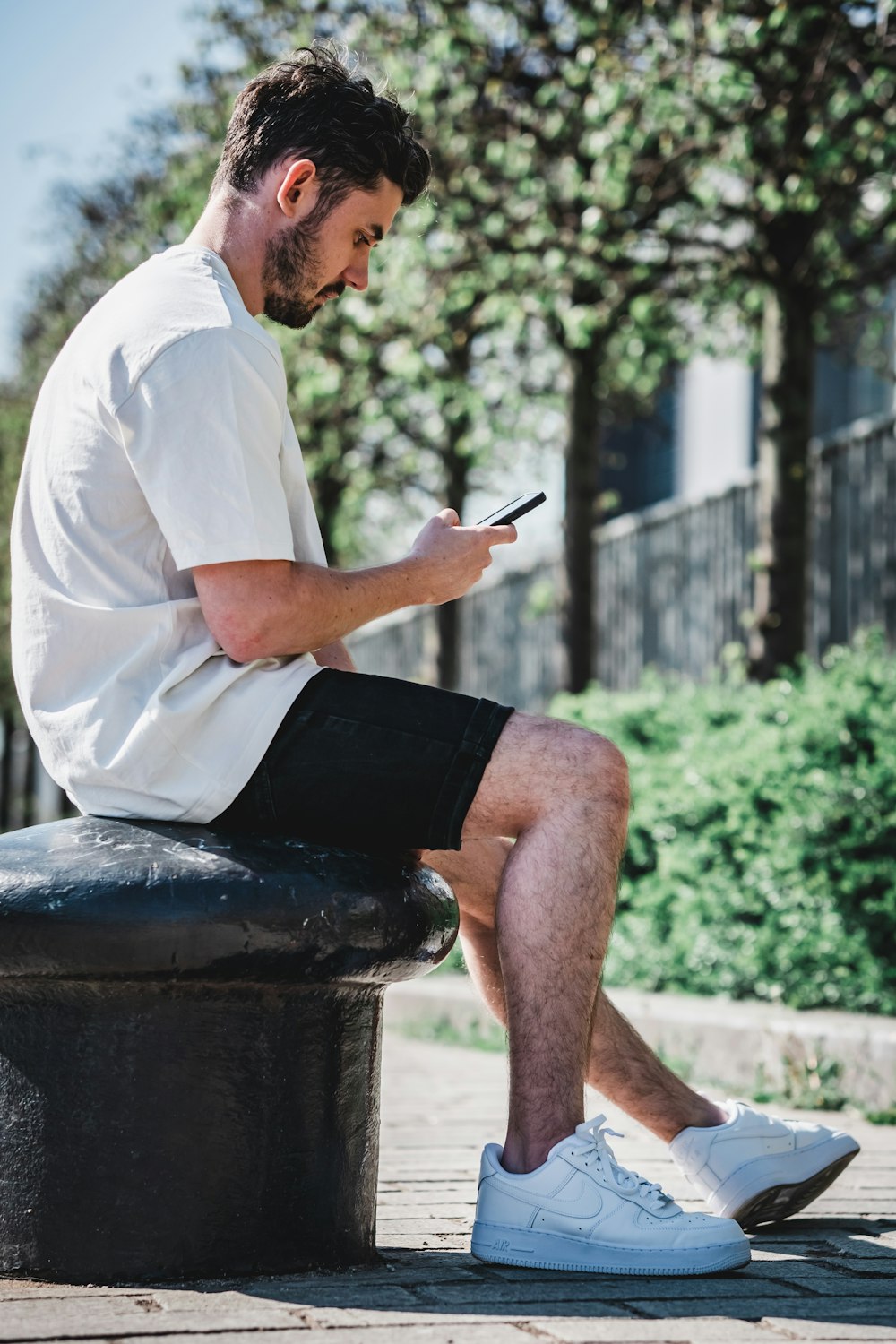 Homme en chemise blanche et short noir assis sur un banc en béton brun pendant la journée