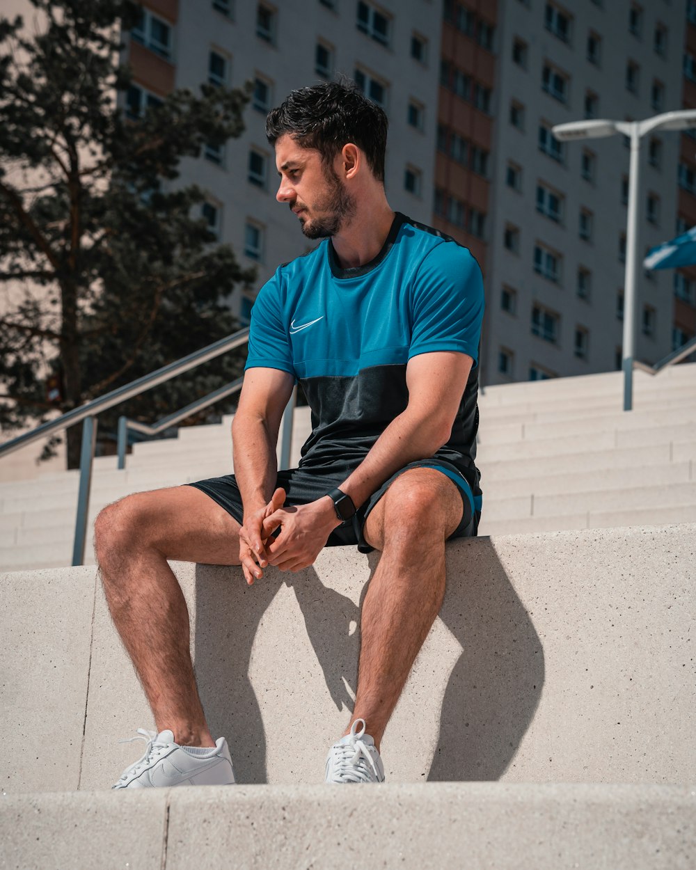 man in blue crew neck t-shirt and black shorts sitting on gray concrete bench during