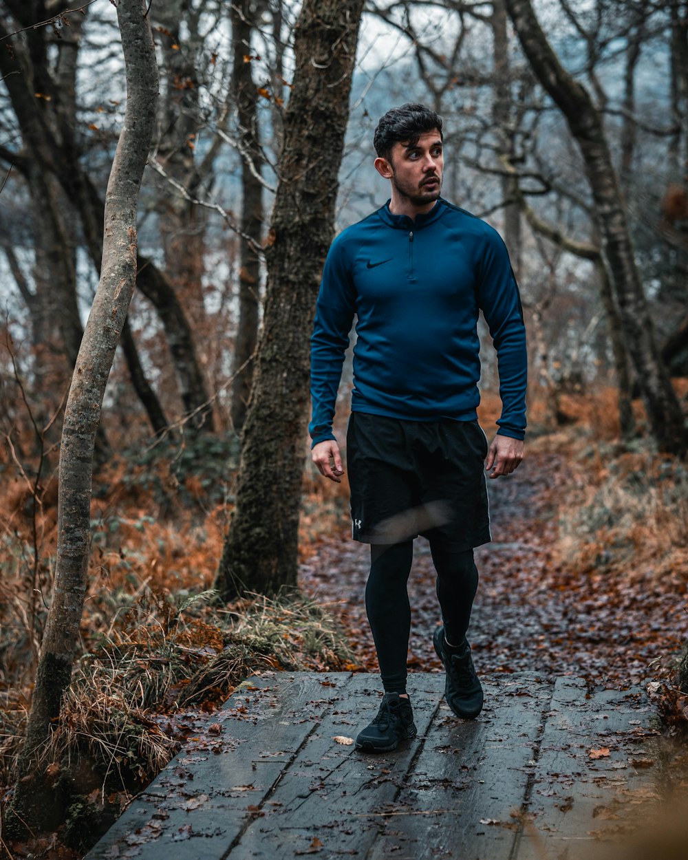 man in blue long sleeve shirt and black pants standing on pathway surrounded by trees during